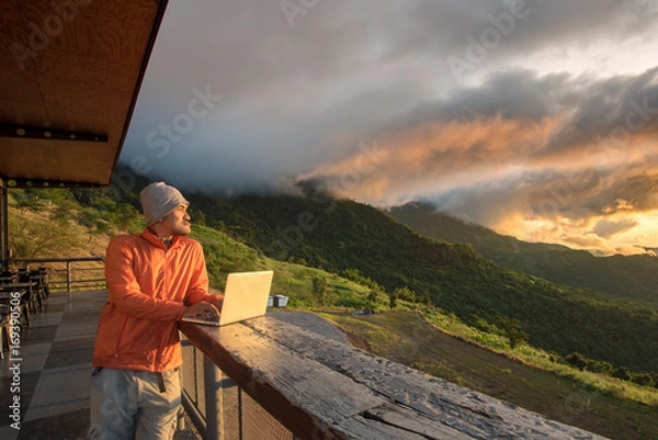 Fototapeta Asian handsome hipster freelance beard man standing, relaxing and working via 5gwireless at mountain cafe during sunrise.
