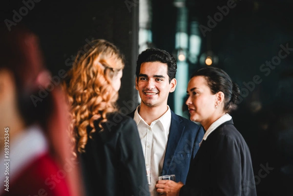 Fototapeta Professionals in formal attire converse and smile at indoor corporate event. Business networking scene includes meeting, conference, seminar, teamwork, discussion, colleagues, and collaboration.