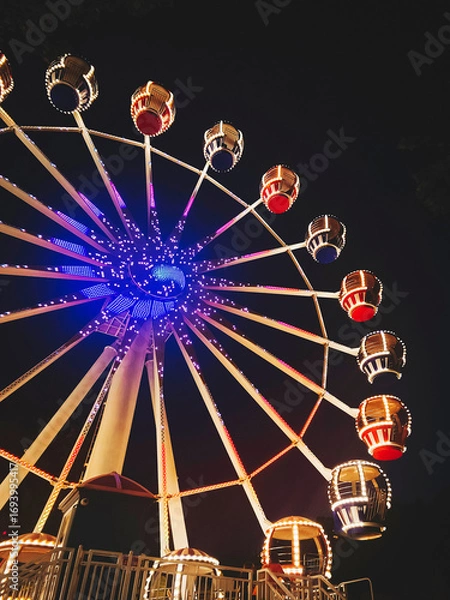 Fototapeta Ferris wheel in amusement park. Beautiful night view with illumination. Vertical photo.