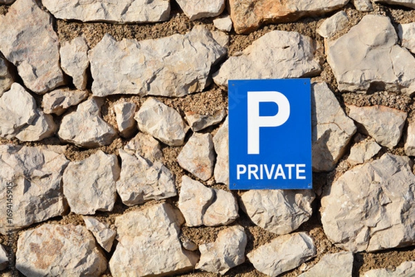 Fototapeta A blue and white private parking sign is mounted on a traditional stone wall, creating a contrast of man-made and natural elements