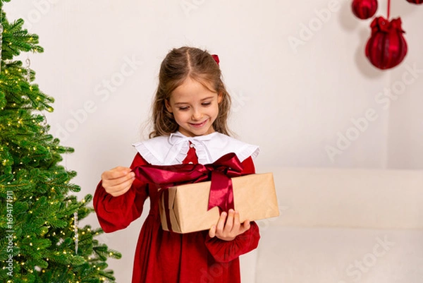 Fototapeta Christmas holidays concept. Happy magic little girl opens a gift box. Child is happy with a New Year's gift. The background is Christmas tree. The concept of Christmas and New Year. High quality photo