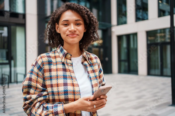 Fototapeta A smiling woman happily using her phone in a vibrant urban setting, radiating positivity and joy