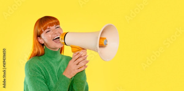 Fototapeta Cheerful young woman with orange hair using a megaphone against a bright yellow background during a lively event in a vibrant studio setting