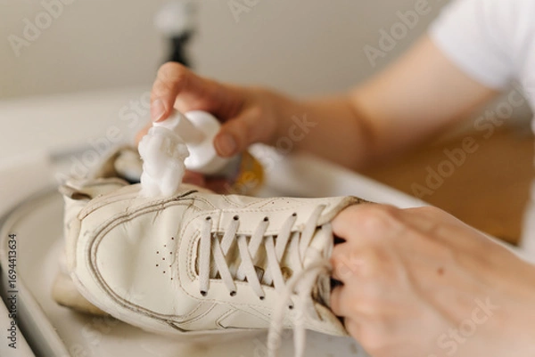 Fototapeta Close-up process of cleaning white sneakers with scrubbing brush and detergent, removing stubborn stains from footwear in basin, preserving shoe hygiene and appearance thorough washing work.