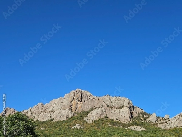 Fototapeta Majestic rocky mountain against a vast, clear blue sky. Perfect for travel themes, motivational content, or as a website banner with ample copy space for text.