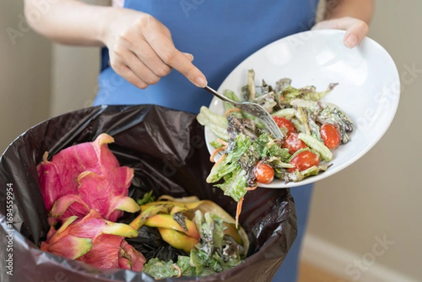 Fototapeta Compost from leftover food housekeeper woman, female hand holding salad dish or plate use fork scraping waste, rotten vegetable throwing away into garbage, trash or bin. Environmentally responsible.