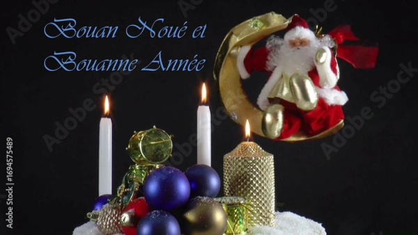 Obraz Warm Wishes for Christmas Joy 
A festive card with candles, baubles, and Santa Claus in the language Jèrriais 
