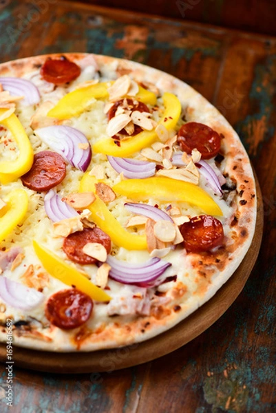 Fototapeta Pizza with chorizo ​​sausage, mozzarella cheese and yellow pepper. Rustic wooden background. Soft focus.	
