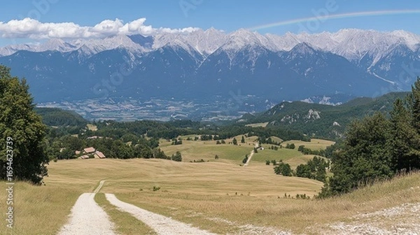 Obraz Panoramic vista of a valley with a dirt road, mountains, and a rainbow