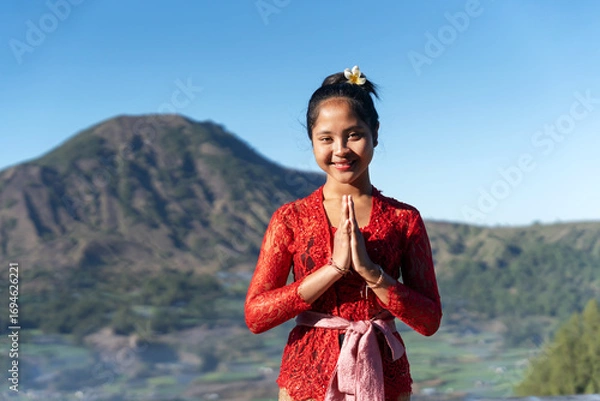 Fototapeta Portrait of Balinese woman hands clasped welcome gesture with Mt. Batur view