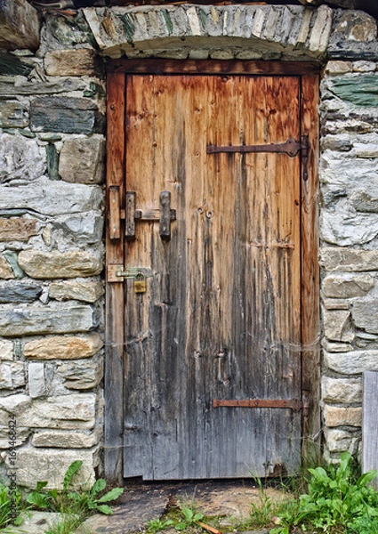 Fototapeta Old wooden door in field stone wall with rusty hinges and padlock