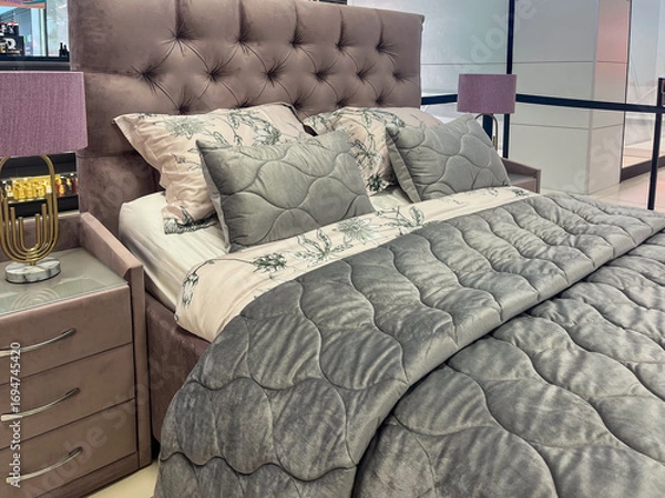 Fototapeta Elegant modern bedroom featuring a plush gray upholstered bed with decorative pillows, cozy quilt, stylish nightstands, and soft lighting creating a serene atmosphere for relaxation