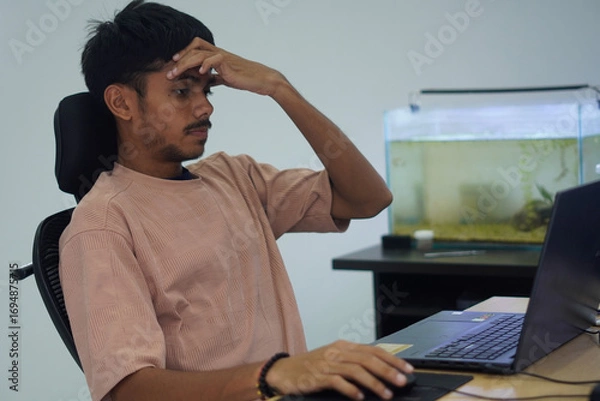 Fototapeta Stressed Man Holding Head While Working on Laptop in Office