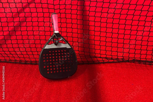 Fototapeta  black padel racket resting on a colored court beside a black net