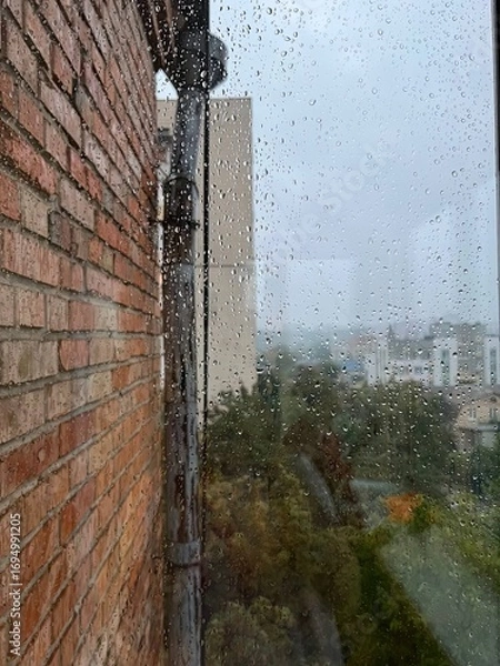 Obraz Rainy day cityscape view through window with raindrops on glass and brick wall creating moody atmosphere