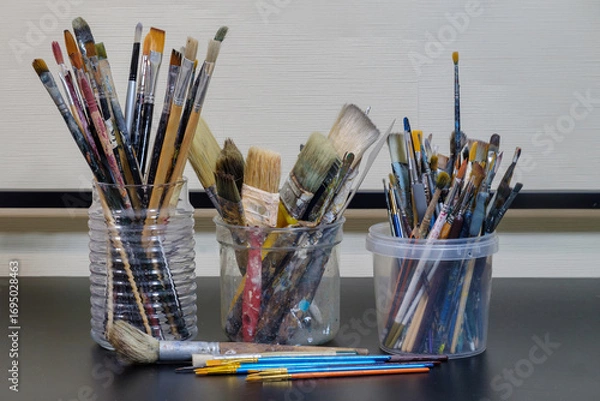Fototapeta Various professional used paint brushes in the jars on a dark surface