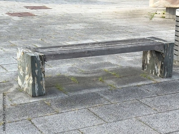Fototapeta Rustic wooden bench with stone supports on paved urban sidewalk