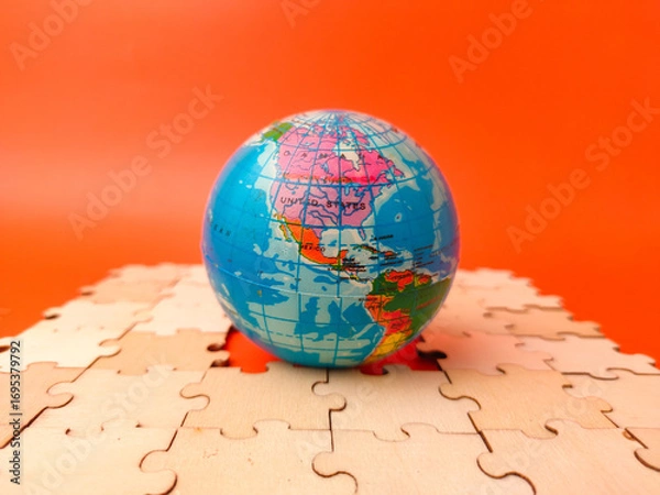 Fototapeta Closeup colorful globe, which is a puzzle, resting on a surface covered with scattered, unassembled puzzle pieces