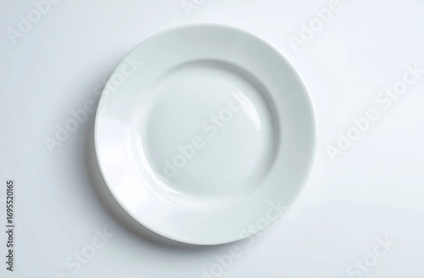 Fototapeta Simple, clean shot of a white, round porcelain plate on a white surface, top-down view, showcasing subtle shadow