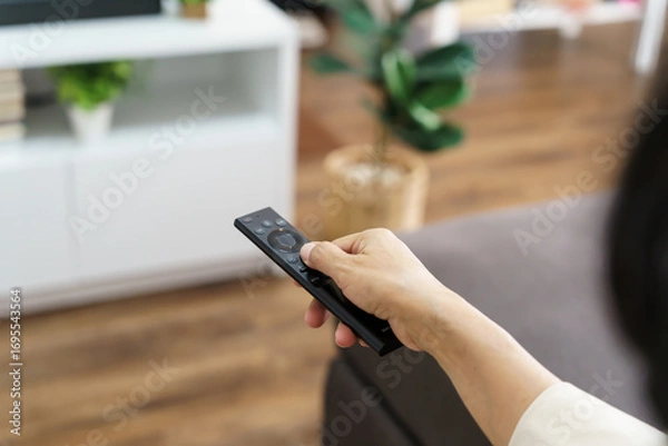 Fototapeta Elderly woman Watching smart TV and using remote controller Hand holding television audio remote control Middle age Asian woman movie Television series spending time at home
