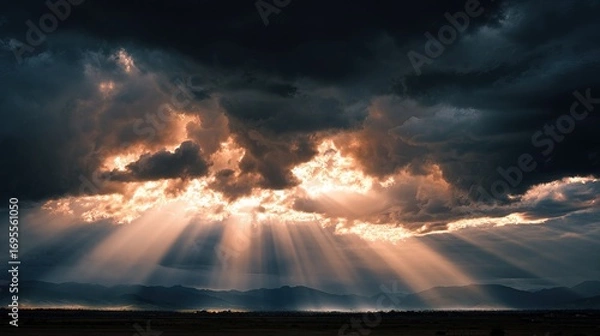 Fototapeta A dramatic sky filled with dark clouds and rays of sunlight breaking through, illuminating the landscape below.