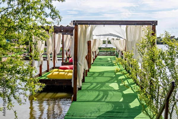 Fototapeta This image shows a serene outdoor setting with a wooden structure that appears to be a gazebo or pavilion