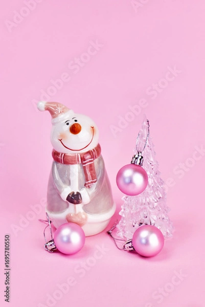 Fototapeta a card with a beautiful transparent Christmas tree decorated with pink balls and a cute snowman next to it, pink background, vertical, creative focus