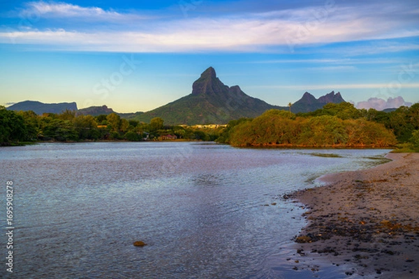 Fototapeta Scenic view of Rempart Mountain from Tamarin Beach, Mauritius, with calm waters in the foreground, lush greenery, and a clear sky at sunset.