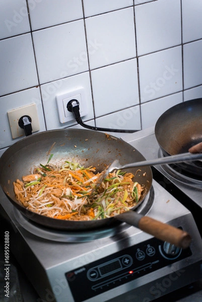 Fototapeta Chef cooking stir-fried vegetables and beef in a wok on a professional kitchen stove. Top-down view of Thai or Asian cuisine in preparation.