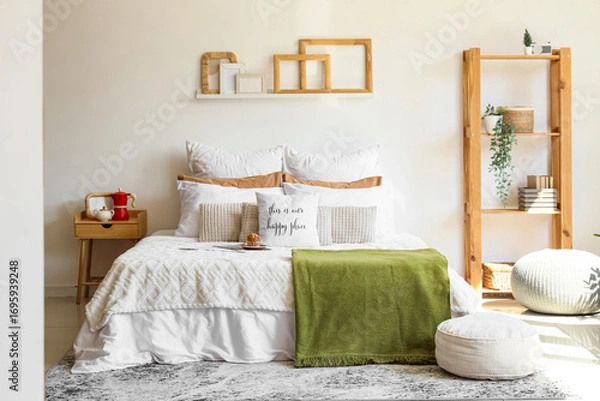 Obraz Big comfortable bed with muffin, bedside table, shelving unit and poufs in interior of bedroom