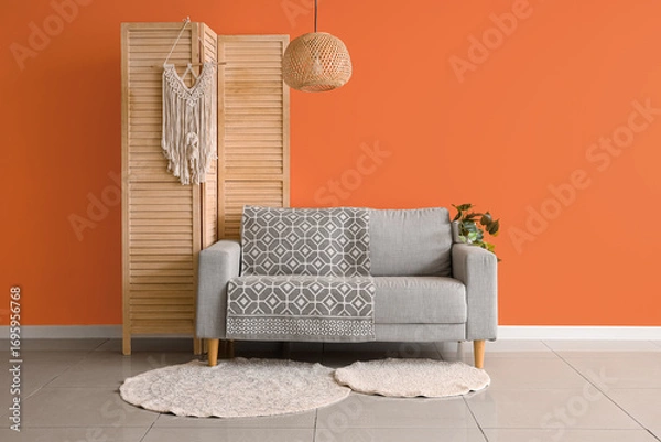 Obraz Comfortable sofa and folding screen near orange wall in interior of living room