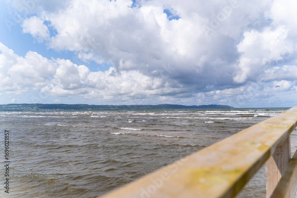Fototapeta A picturesque wooden pier gracefully extending into the vast ocean beneath a vibrant sky and gentle waves, Bastad, Sweden
