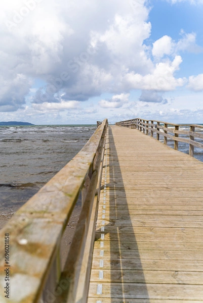 Fototapeta A picturesque wooden pier gracefully extending into the vast ocean beneath a vibrant sky and gentle waves, Bastad, Sweden