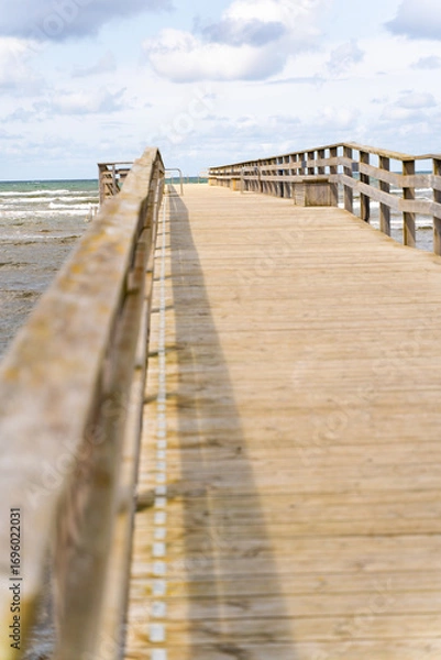 Fototapeta A picturesque wooden pier gracefully extending into the vast ocean beneath a vibrant sky and gentle waves, Bastad, Sweden