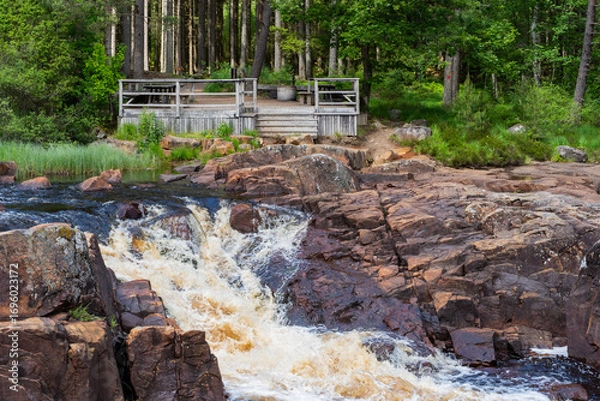 Fototapeta A Serene River Scene Featuring Cascading Water Flowing Through a Lush Green Forest