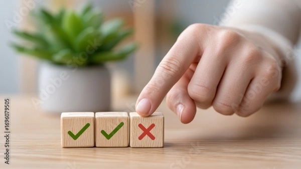 Fototapeta A hand points at three wooden blocks, two marked with check marks and one with a cross, alongside a decorative green plant.