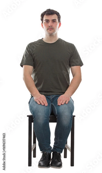 Fototapeta Full length portrait of casual young man sitting on a chair, hands on knees, looking serious to camera isolated on transparent background