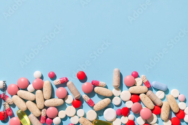 Fototapeta Concept of health and medicine, healthcare and pharmacology. Different multi-colored tablets, vitamins, pills on blue background close-up. Dietary supplements and homeopathy background