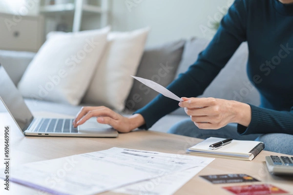 Fototapeta Stressed asian young business woman, employee using laptop computer to calculate expenses, hand holding bills and receipt for to payment on table at home. Financial, finance of banking concept.