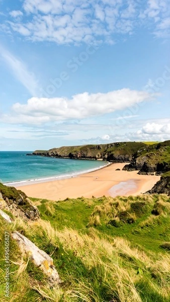 Fototapeta A beautiful beach scene with a vast expanse of sand, surrounded by lush green hills, under a vibrant blue sky dotted with fluffy white clouds.