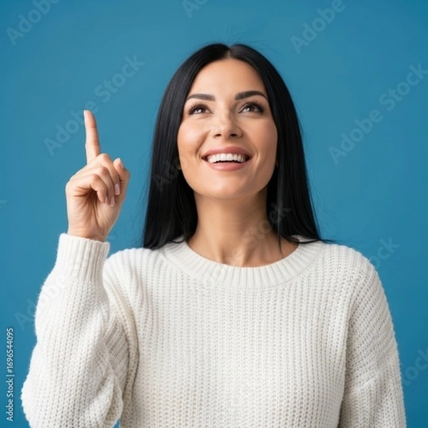 Obraz Young woman points upwards with a smile against a blue background
