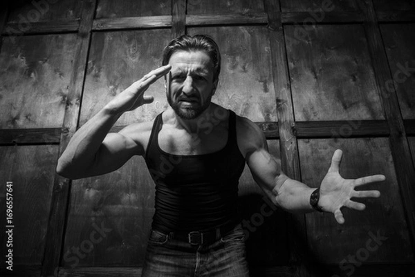 Fototapeta Under a dim light, a muscular man showcases his raw emotions, combining strength with tenderness as he passionately conveys his feelings in a rustic setting, highlighting an unexpected romance.