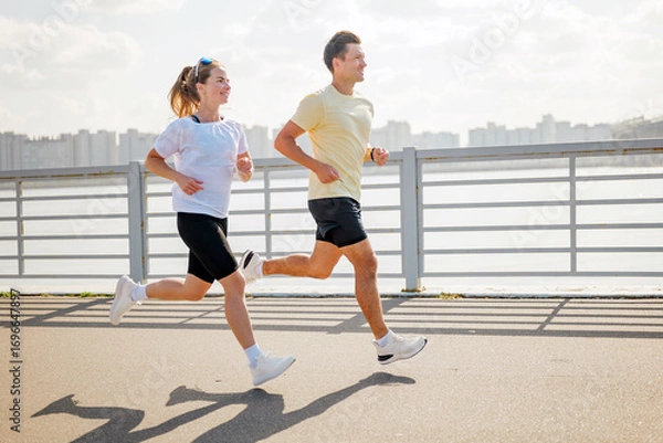 Fototapeta Couple jogging along waterfront path while enjoying fitness and fresh air in a bustling urban environment
