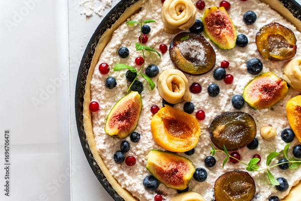 Fototapeta Raw tart or open summer pie with figs, prunes, apricots and blueberries is ready to bake in a round mold. Close-up. View from above. High quality photo