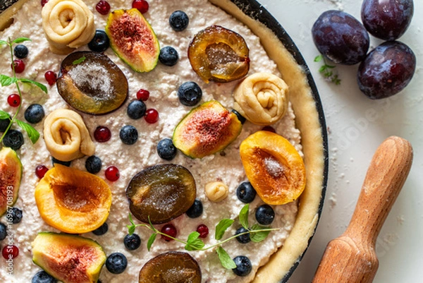 Fototapeta Raw tart or open summer pie with figs, prunes, apricots and blueberries is ready to bake in a round mold. Close-up. View from above. High quality photo