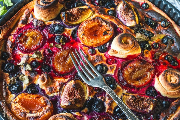 Fototapeta A tart or open pie with blueberries, figs, prunes and apricots in a baking dish on a gray background with a fork. High quality photo