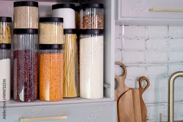 Obraz Organized kitchen pantry with cylindrical plastic jar for storing loose products,  in grey tones