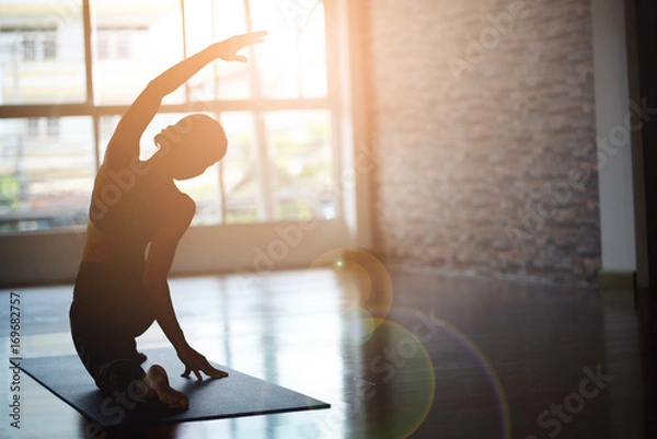 Fototapeta Asian woman doing yoga in a room with sunlight coming through the window.