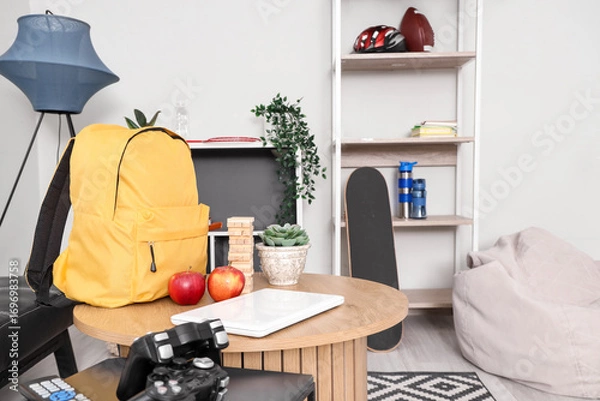Fototapeta Yellow backpack with apples, laptop and game on table in children's room