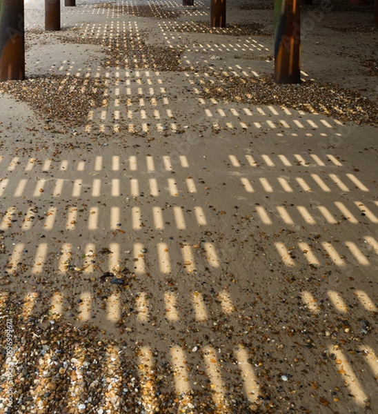 Fototapeta Shadow patterns on the beach under a Pier for use as a background texture